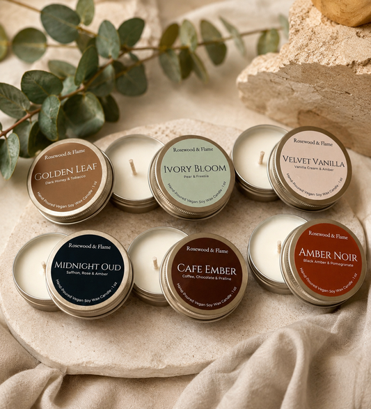 Six open round candle tins arranged on a stone slab with draped fabric and decorative leaves. The tins show different scent labels including Golden Leaf, Ivory Bloom, Velvet Vanilla, Midnight Oud, Cafe Ember, and Amber Noir.
