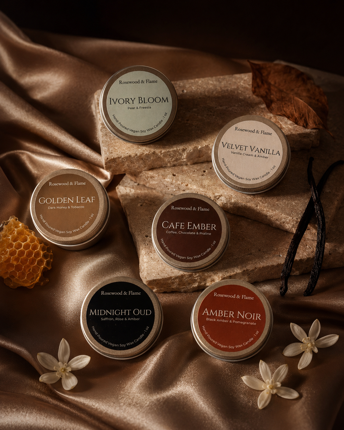 Six round mini tin container candles arranged on draped satin fabric with stone blocks and natural props. The lids show the brand Rosewood & Flame and the scent names Ivory Bloom, Velvet Vanilla, Golden Leaf, Cafe Ember, Midnight Oud, and Amber Noir.